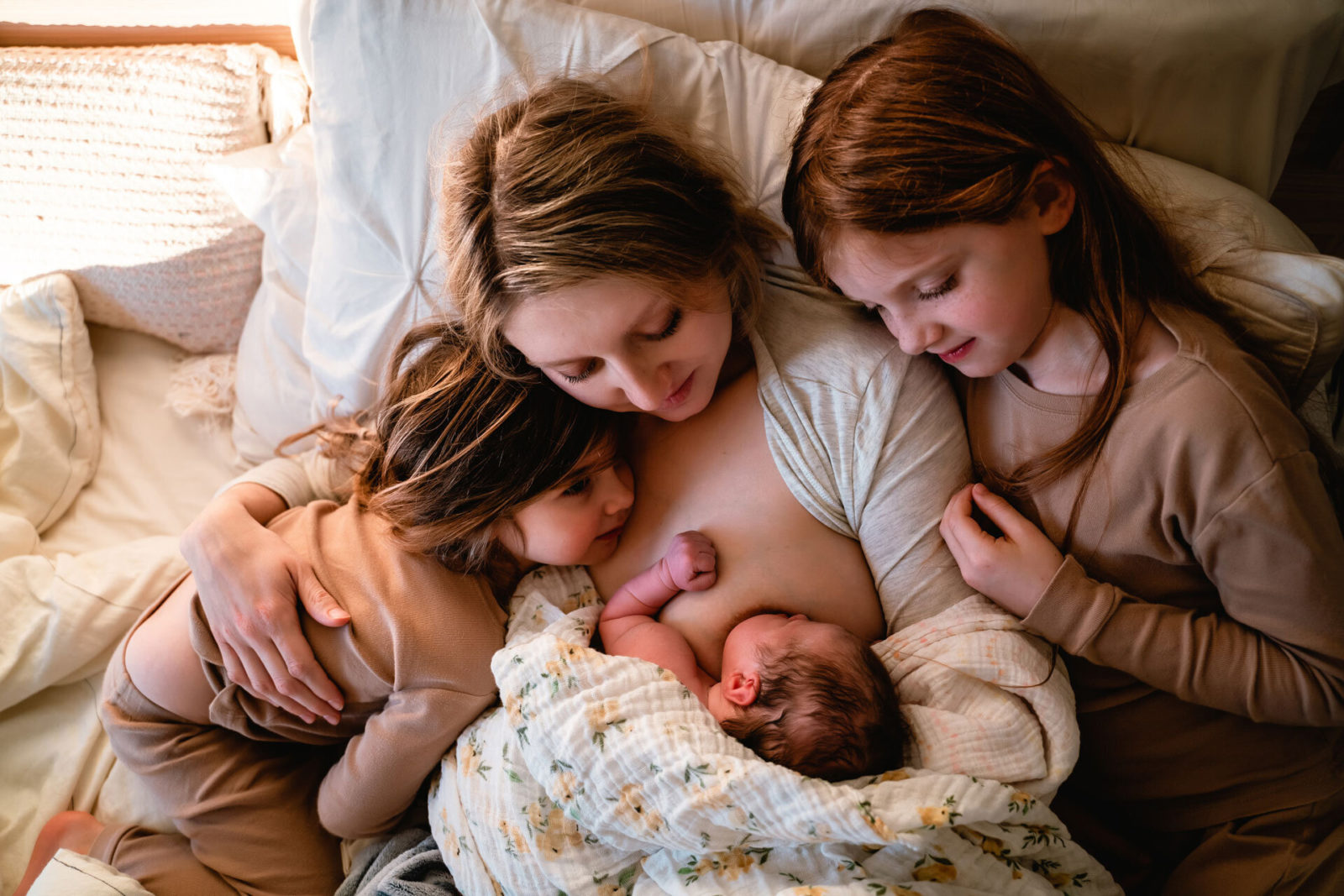 mother snuggles newborn and two daughters after birth