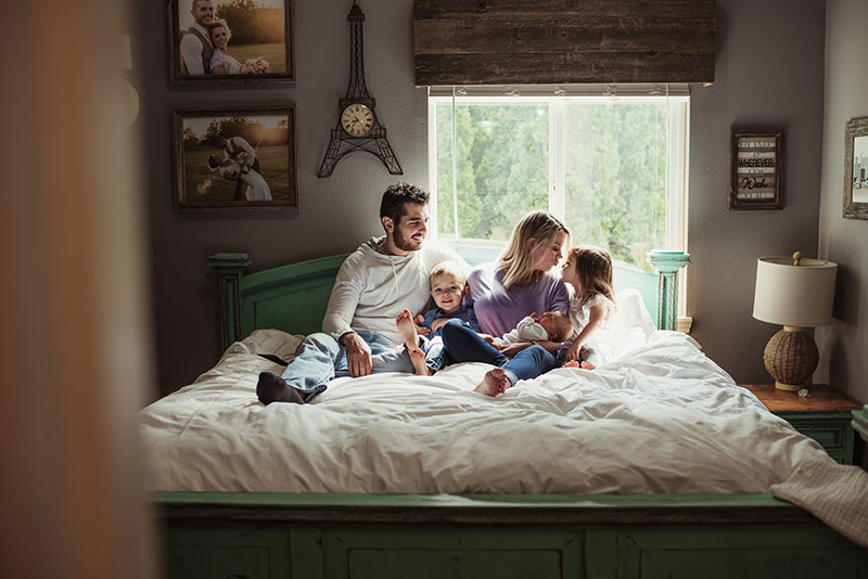 Parents and their newborn baby in bed with two siblings during Lifestyle Newborn session in Beaverton, Oregon