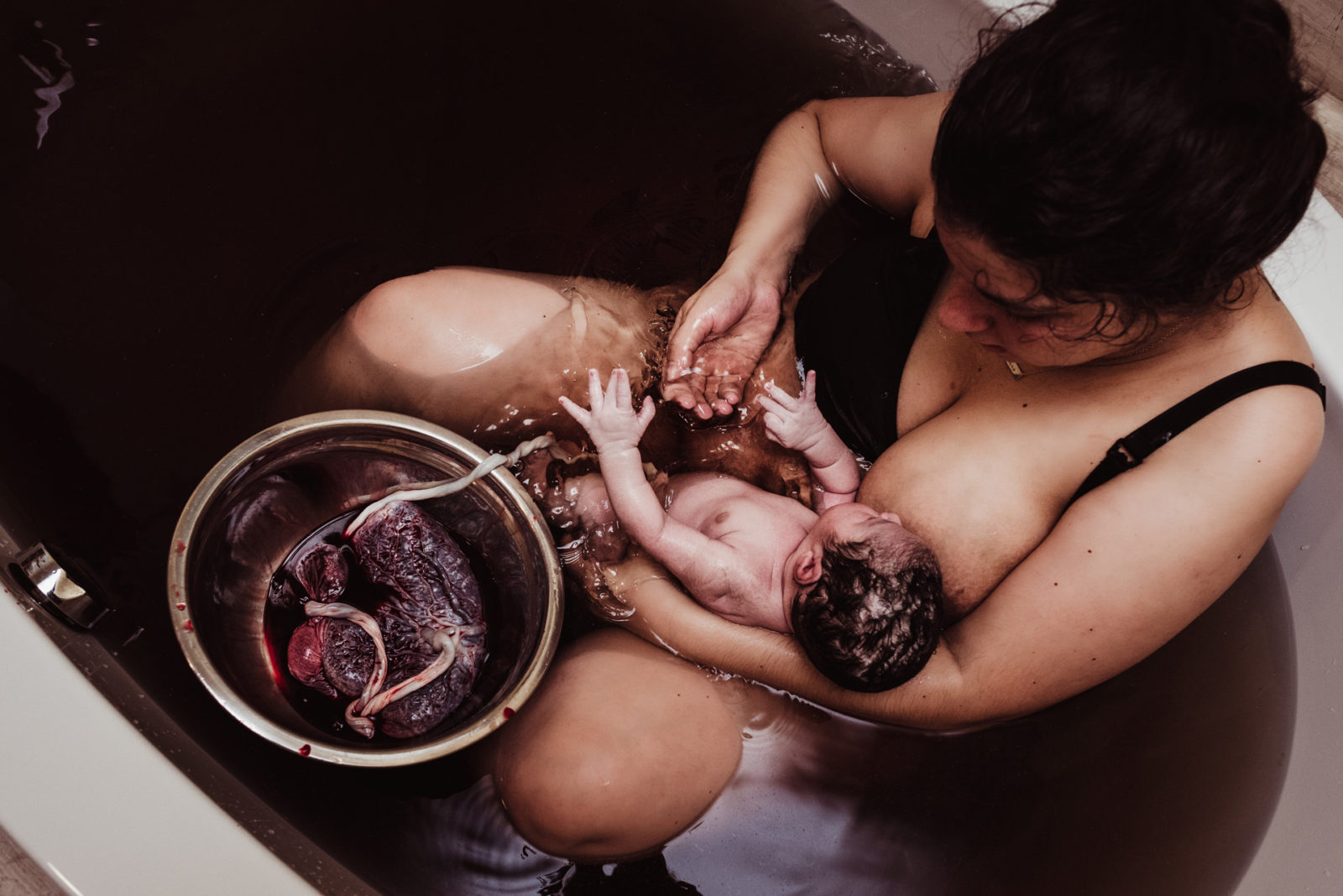 mother holding baby in water with placenta floating nearby