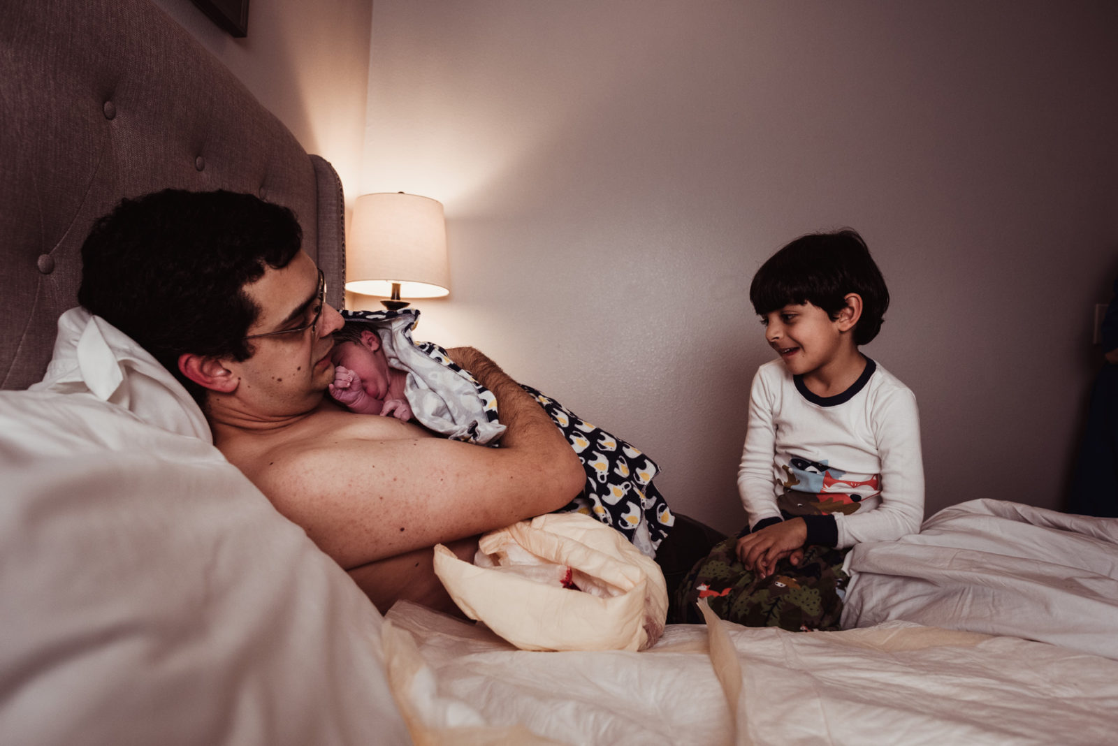 father and son with their newborn baby in bed after birth