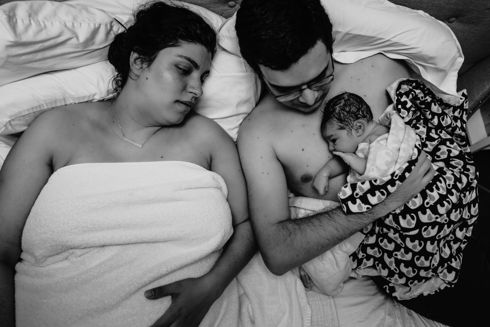 mother and father with their newborn in bed after birth
