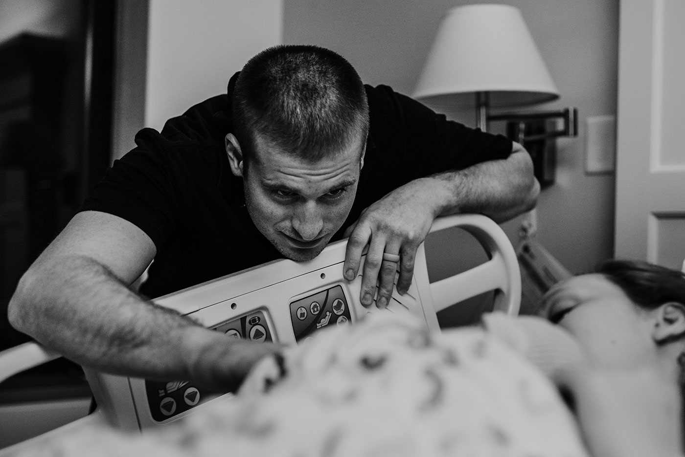 dad looks lovingly at his baby just born laying on mom's chest in hospital bed