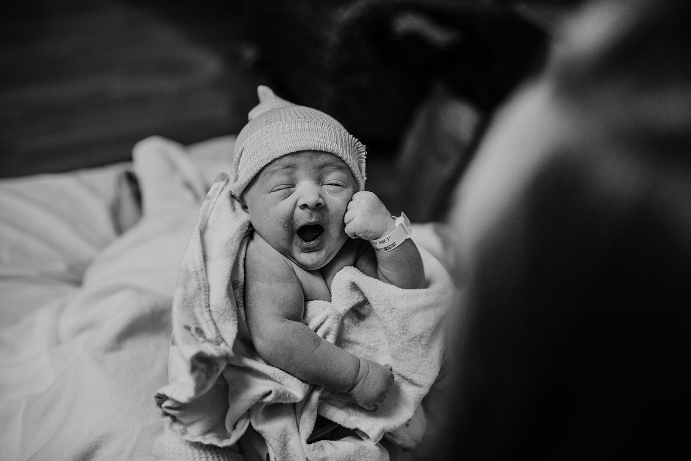 newborn baby boy yawns while mom looks down at him after birth