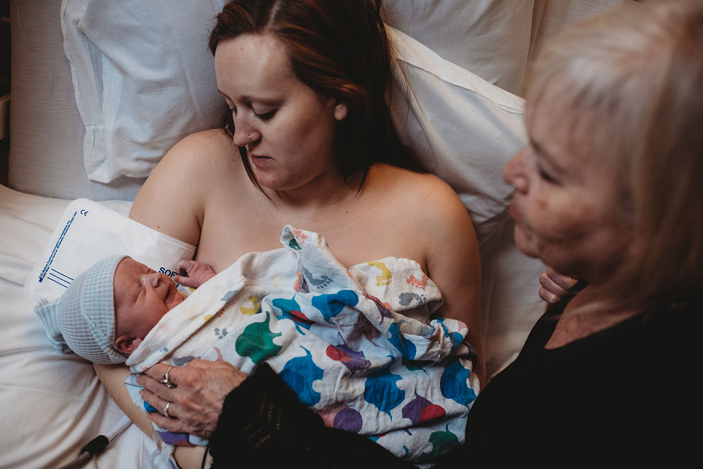 great-grandma gently touches newborn baby boy doing skin to skin with mom in bed