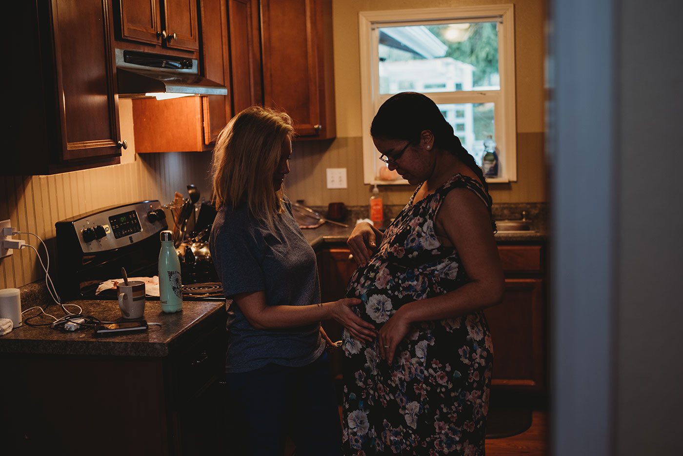 a doula touches mom's belly in her kitchen - home birth photography