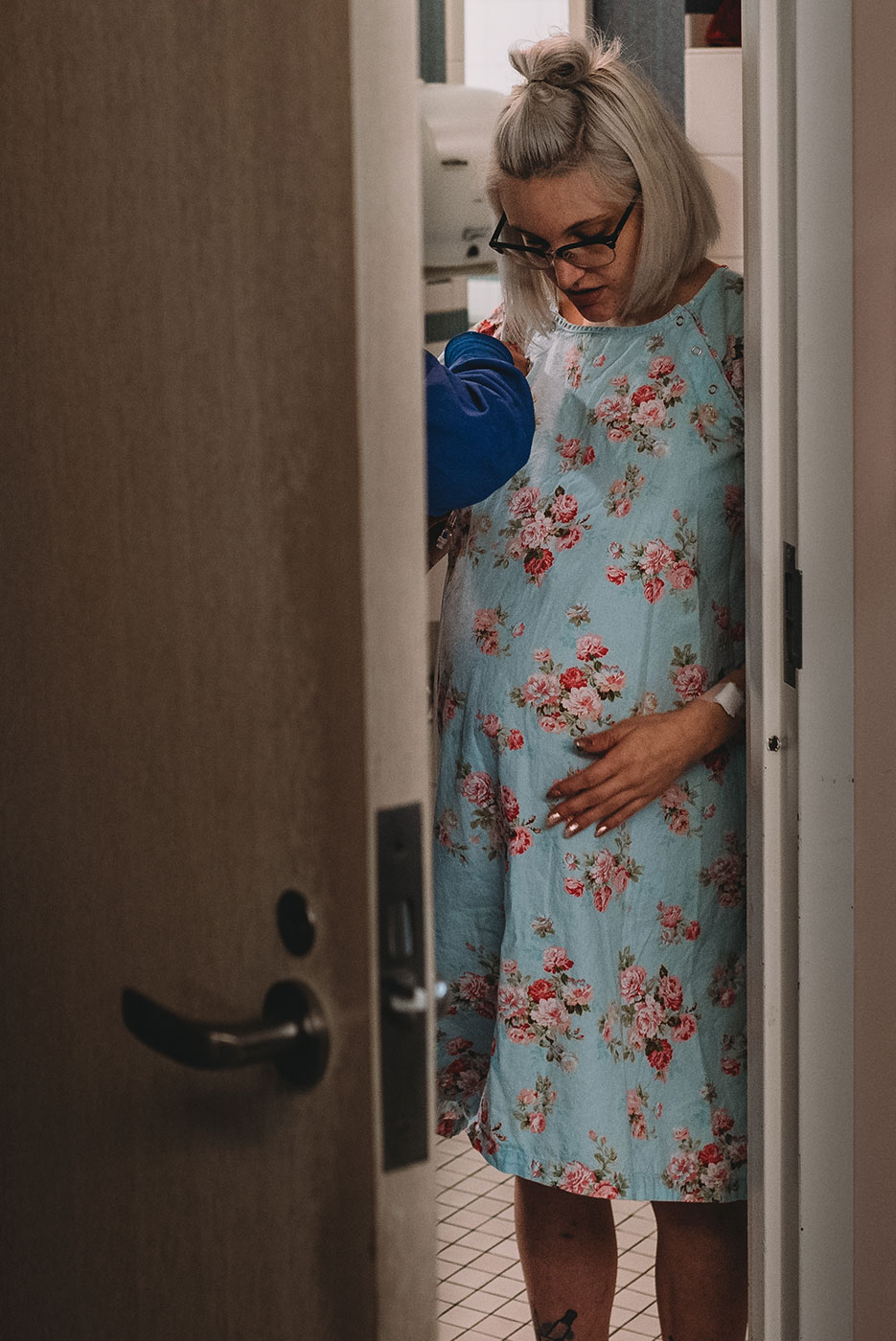 mom stands up in the doorway of the hospital room and touches her pregnant belly