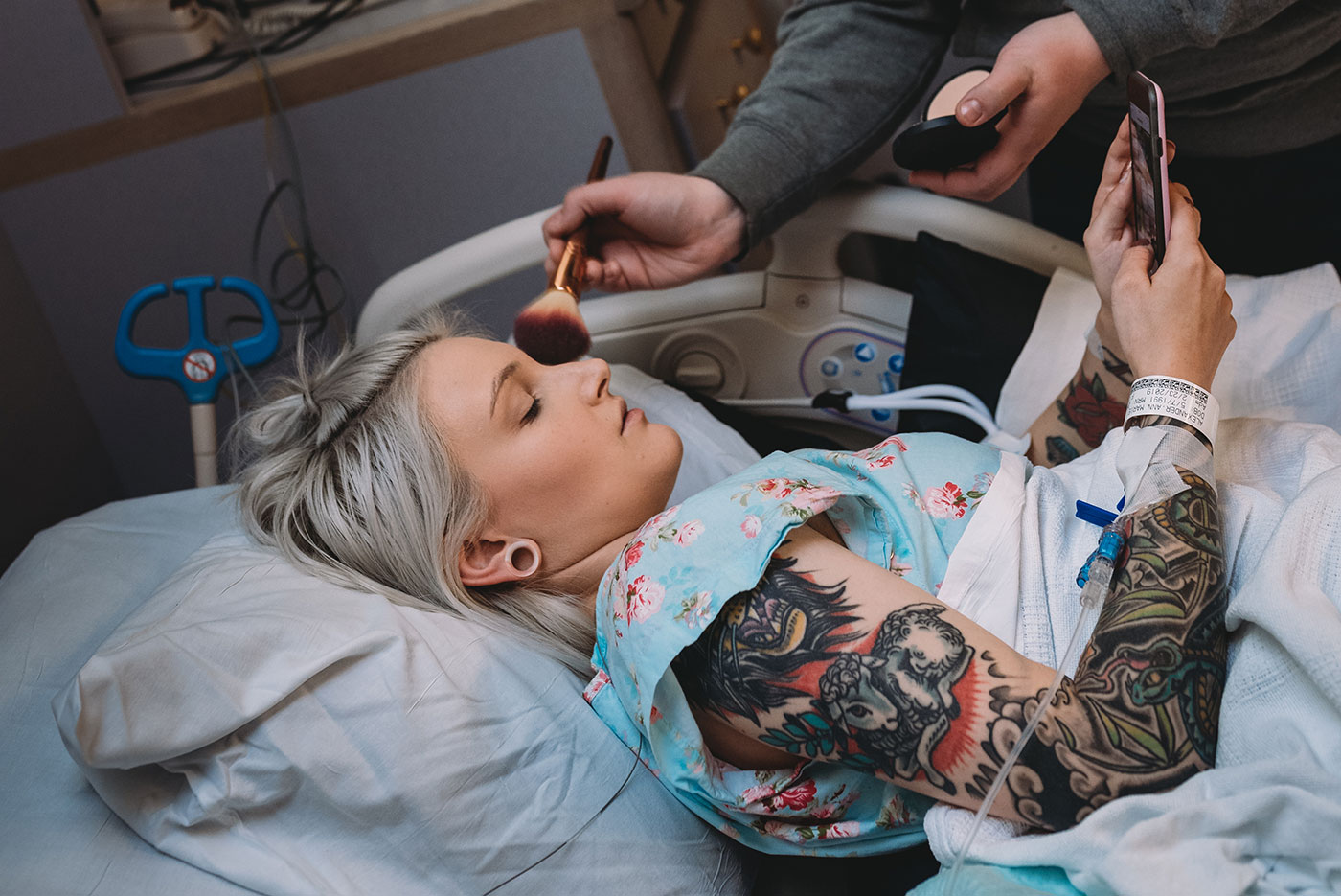 tattooed mom laying in hospital bed having makeup applied before birth
