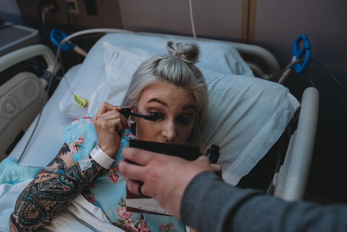 tattooed mom applies mascara in the mirror during birth in the hospital