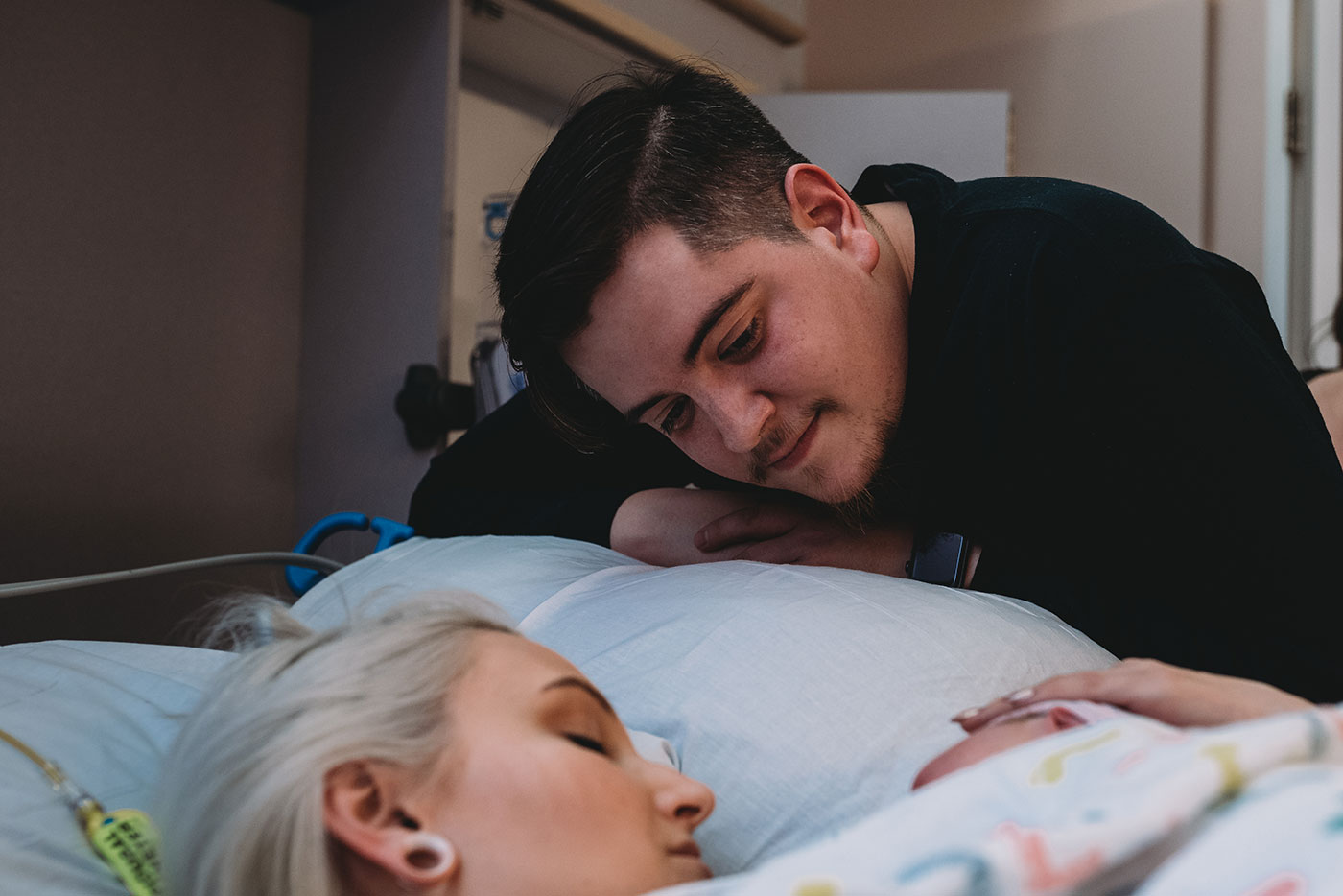 dad leans over to look at his new baby while mom does skin to skin after birth