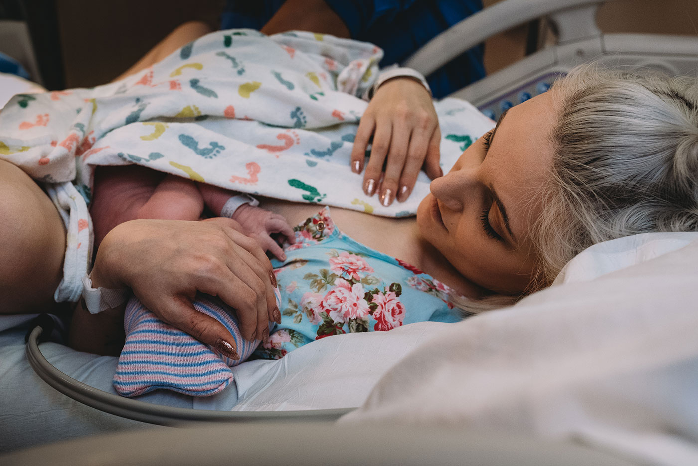 mom looks down at her newborn baby wearing a pink and blue striped hat