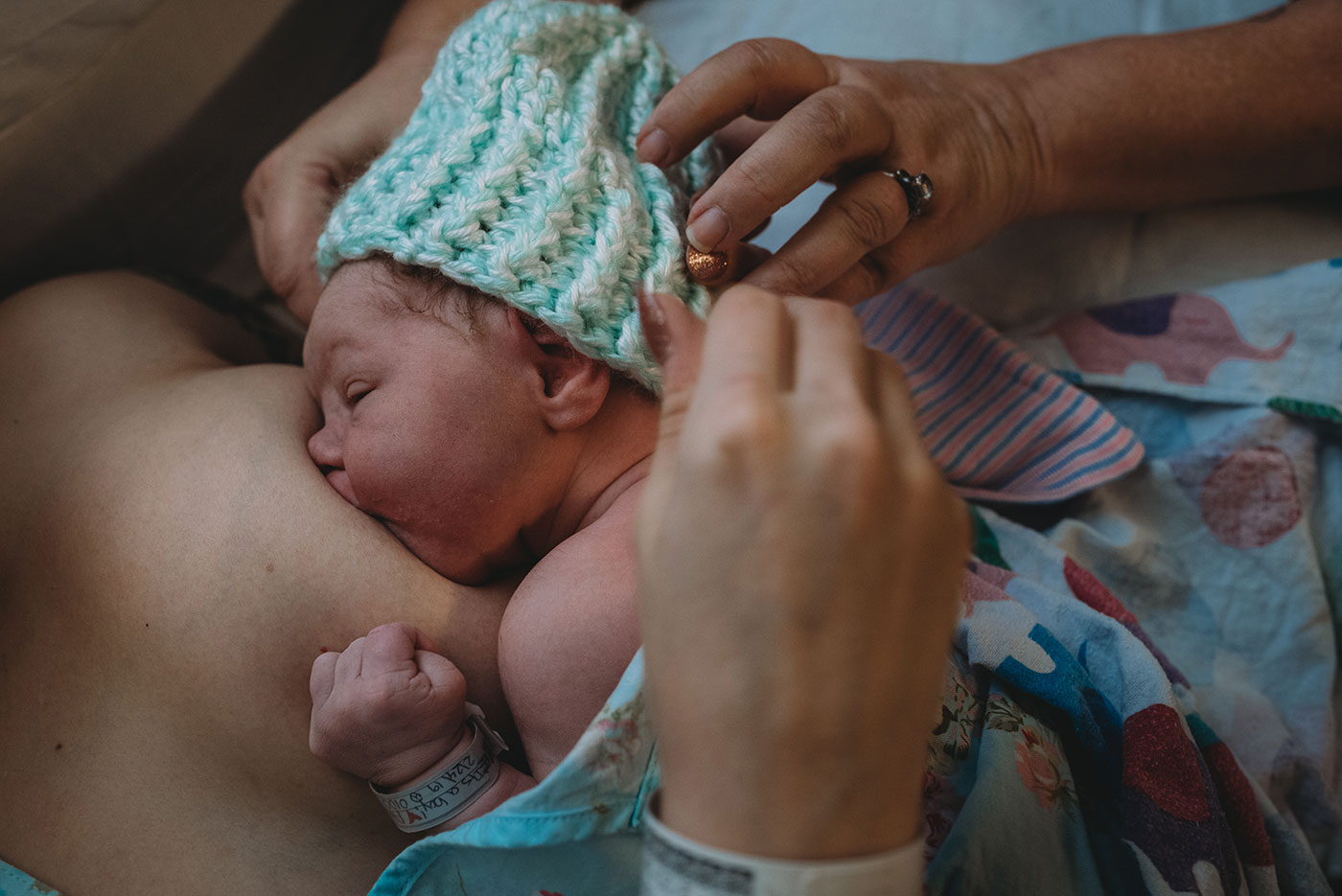 grandma puts a hand-made hat on breastfeeding baby's head after birth