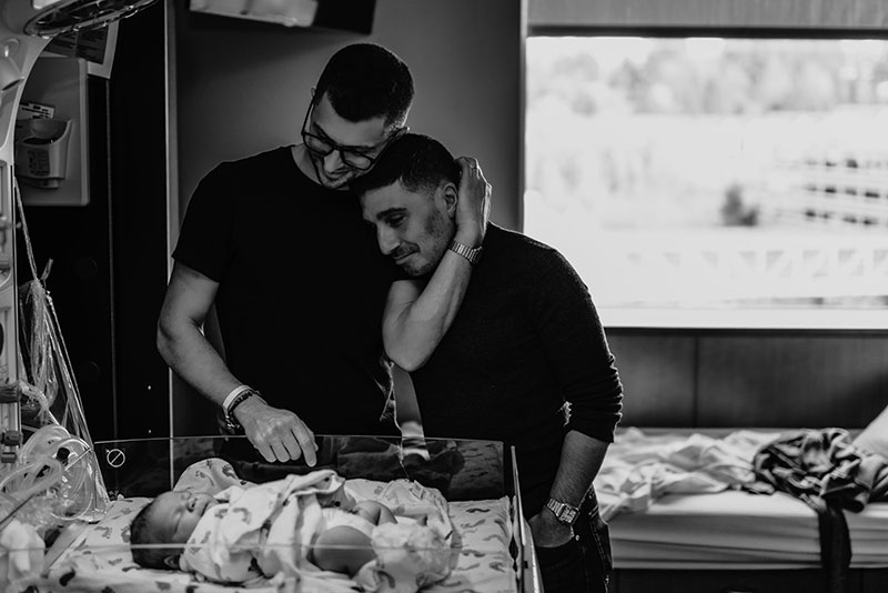 two dads looking at their newborn baby