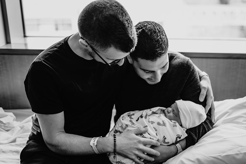two dads holding their newborn baby for the first time