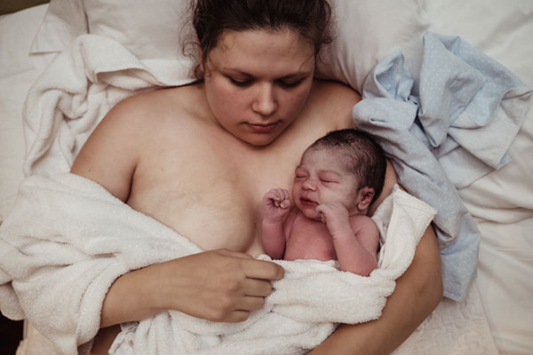 mother holds her newborn in white sheets