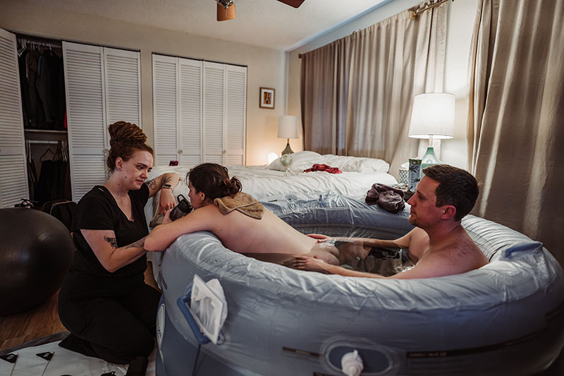 doula Natalie Broders offering water to a person in a birth tub with their partner in labor